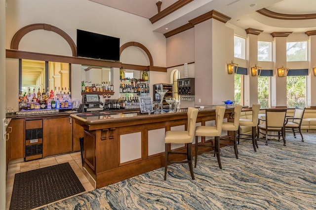 bar with light tile flooring, a raised ceiling, and a towering ceiling