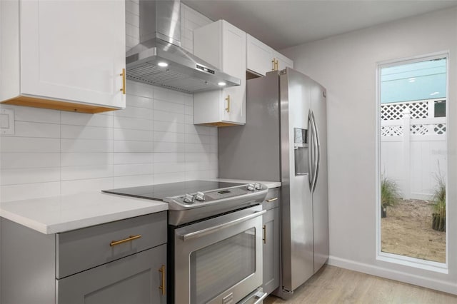 kitchen featuring backsplash, wall chimney exhaust hood, light hardwood / wood-style floors, and range with electric stovetop