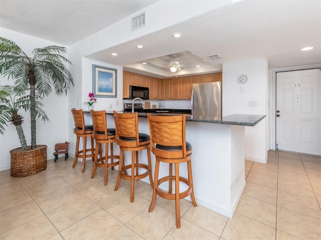 kitchen featuring a kitchen bar, a tray ceiling, ceiling fan, stainless steel refrigerator, and light tile patterned flooring