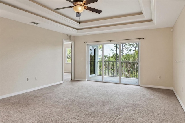 empty room with a raised ceiling, ceiling fan, and light carpet