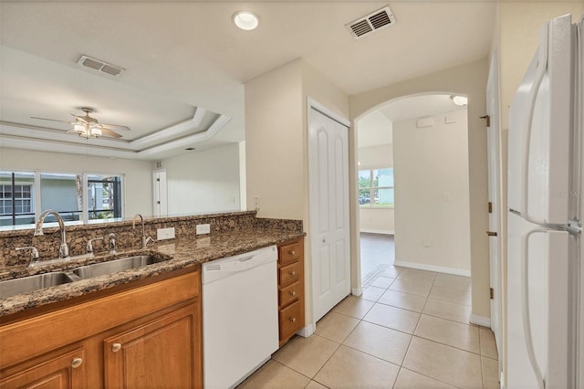 kitchen featuring dark stone counters, a healthy amount of sunlight, a raised ceiling, and white appliances