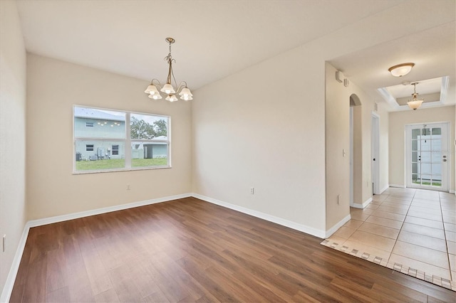 unfurnished room with an inviting chandelier, light hardwood / wood-style floors, and a tray ceiling