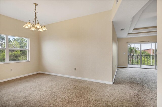 empty room with a tray ceiling, a healthy amount of sunlight, light colored carpet, and a chandelier