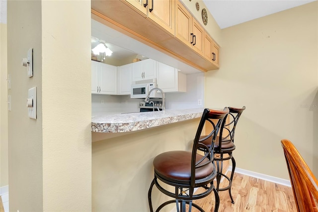 kitchen with a kitchen breakfast bar, white cabinetry, and light hardwood / wood-style floors