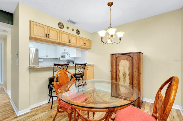 dining space with light wood-type flooring, baseboards, visible vents, and a chandelier