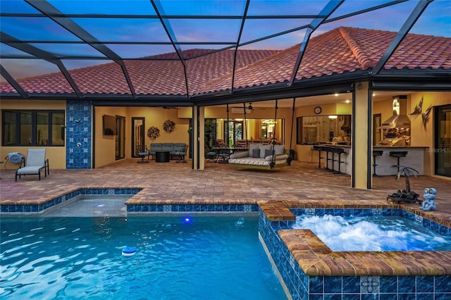 pool at dusk with an in ground hot tub, an outdoor hangout area, pool water feature, a bar, and a patio