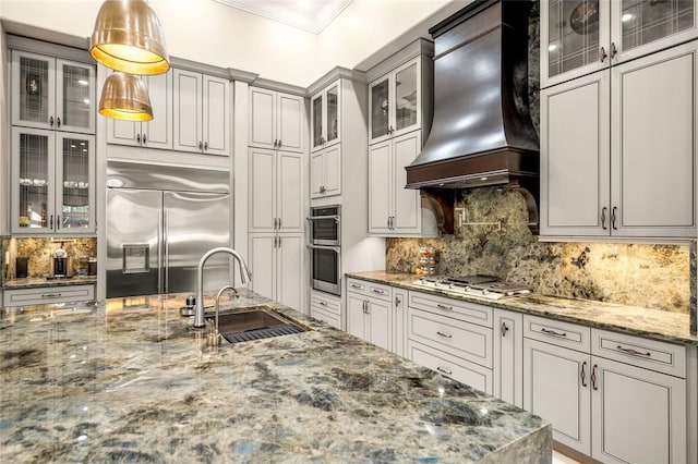 kitchen featuring backsplash, premium range hood, sink, appliances with stainless steel finishes, and decorative light fixtures