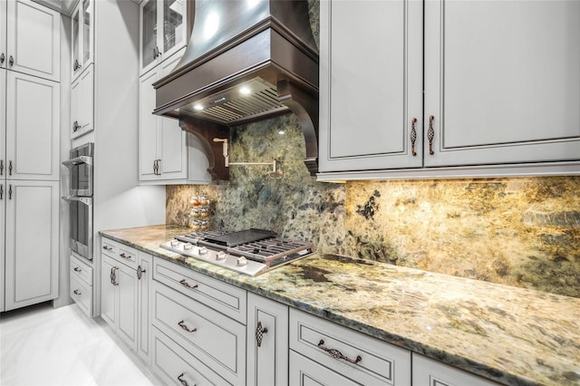 kitchen featuring light stone countertops, tasteful backsplash, stainless steel gas cooktop, and custom exhaust hood