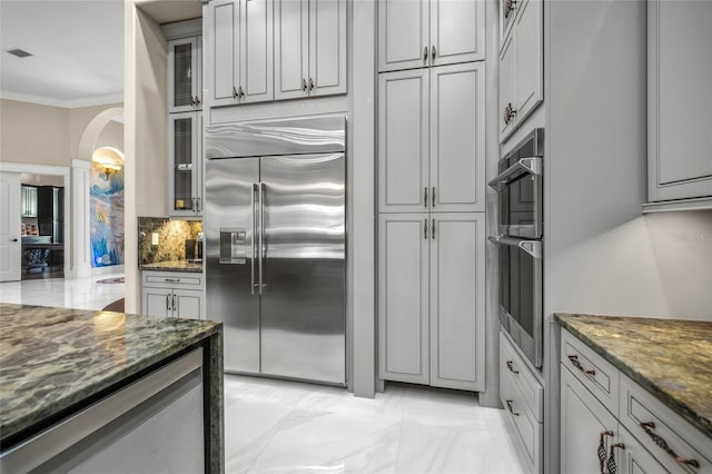 kitchen with tasteful backsplash, dark stone countertops, gray cabinets, and appliances with stainless steel finishes