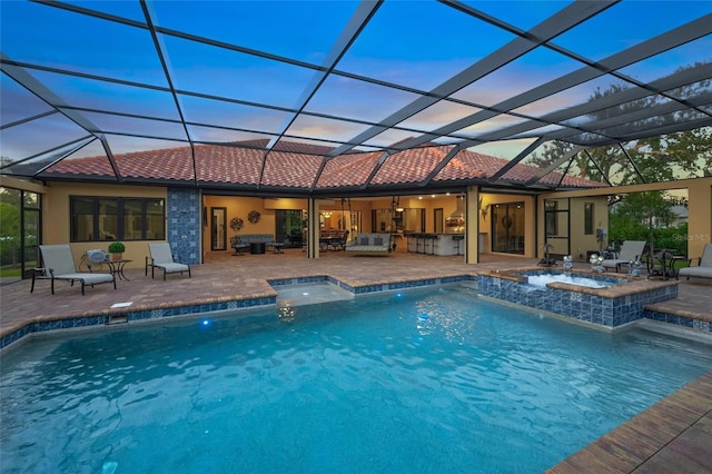 pool at dusk with a lanai, an in ground hot tub, a patio, and an outdoor kitchen