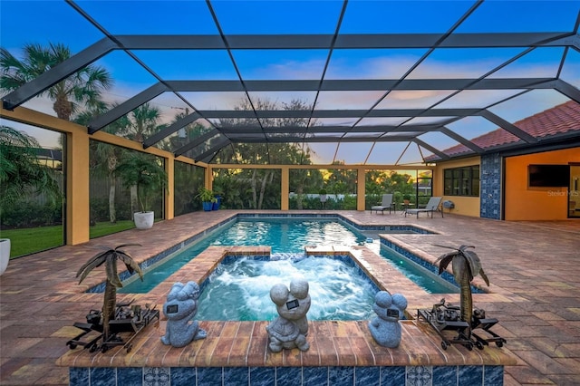 pool at dusk featuring glass enclosure, an in ground hot tub, a patio area, and pool water feature