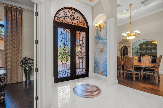 foyer with hardwood / wood-style flooring, a notable chandelier, ornamental molding, and french doors