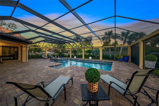 pool at dusk featuring a lanai, an in ground hot tub, and a patio