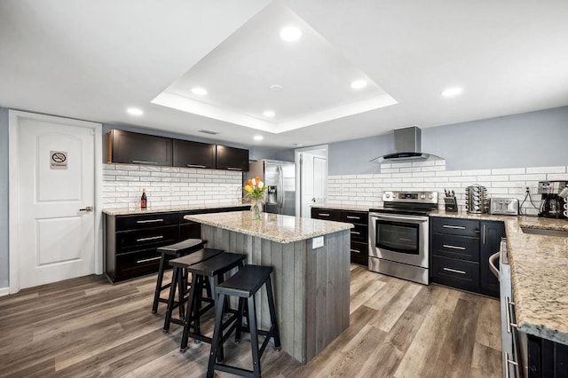 kitchen with appliances with stainless steel finishes, a center island, light wood-type flooring, and ventilation hood