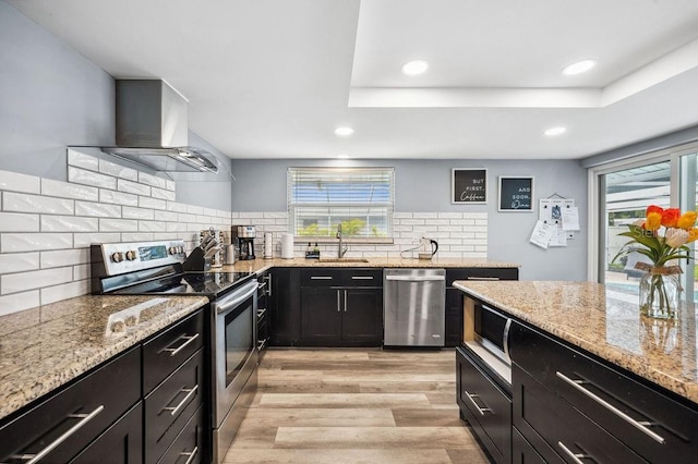 kitchen with appliances with stainless steel finishes, wall chimney range hood, plenty of natural light, and light wood-type flooring