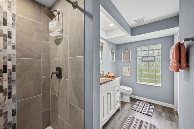 bathroom with tiled shower, wood-type flooring, toilet, and vanity