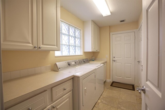 clothes washing area featuring washing machine and clothes dryer, sink, cabinets, a textured ceiling, and light tile patterned floors