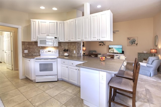 kitchen with tasteful backsplash, white cabinets, a kitchen breakfast bar, kitchen peninsula, and white appliances