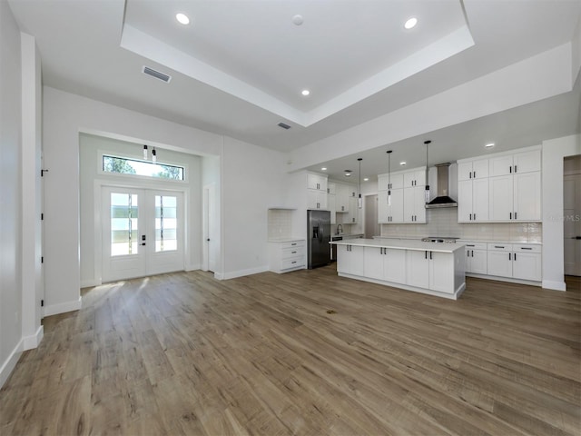 unfurnished living room with wood-type flooring, a tray ceiling, and french doors