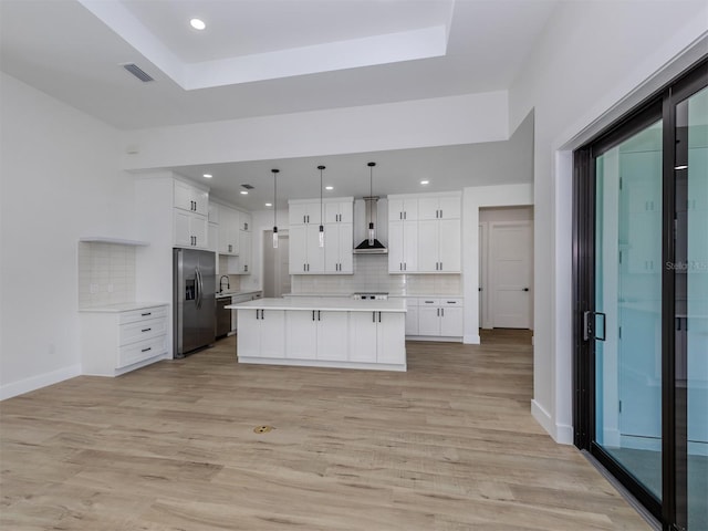 kitchen with light wood-type flooring, wall chimney range hood, white cabinetry, and stainless steel refrigerator with ice dispenser