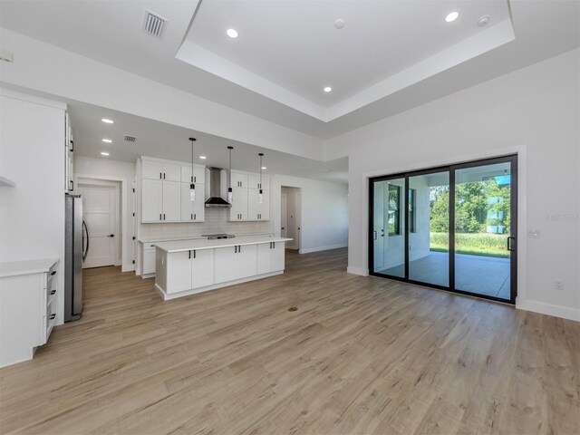 kitchen featuring light hardwood / wood-style floors, wall chimney exhaust hood, white cabinetry, hanging light fixtures, and a raised ceiling