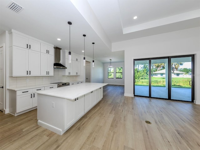 kitchen with white cabinets, a kitchen island, stainless steel electric stove, light wood-type flooring, and wall chimney exhaust hood