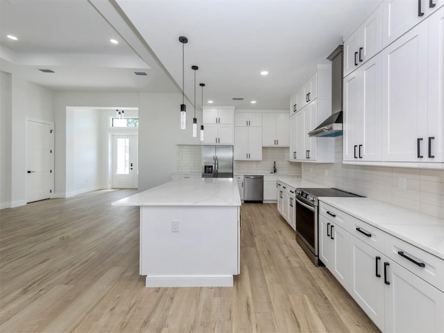 kitchen featuring appliances with stainless steel finishes, light wood-type flooring, a center island, decorative light fixtures, and white cabinetry