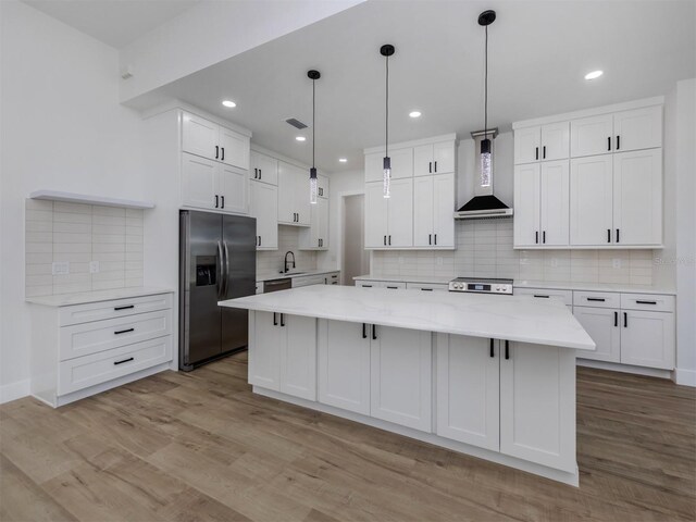 kitchen featuring backsplash, stainless steel refrigerator with ice dispenser, pendant lighting, and wall chimney exhaust hood