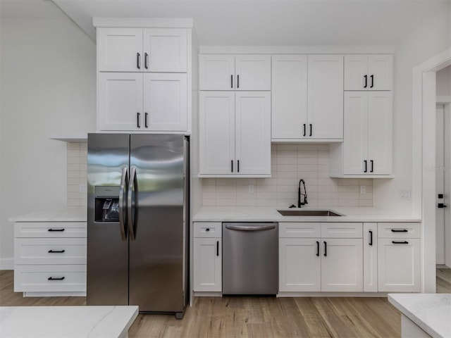 kitchen featuring tasteful backsplash, white cabinetry, stainless steel appliances, light wood-type flooring, and sink