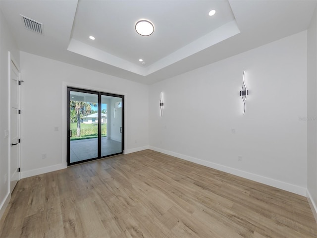 spare room featuring a tray ceiling and light hardwood / wood-style floors