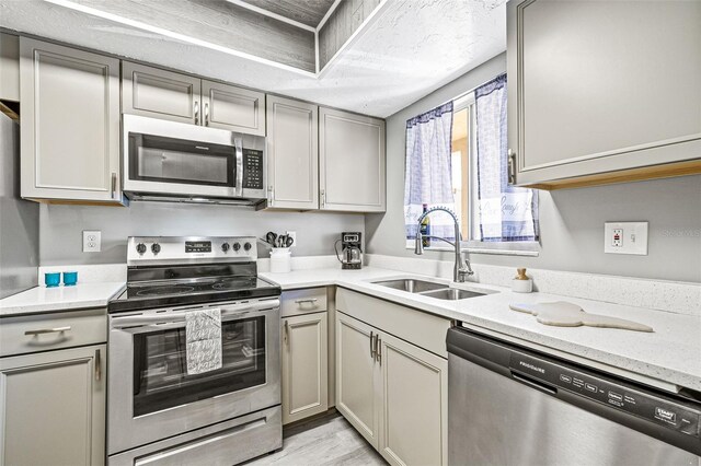 kitchen with a textured ceiling, stainless steel appliances, light wood-type flooring, gray cabinetry, and sink