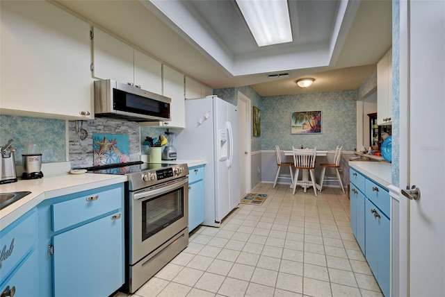 kitchen with white cabinets, backsplash, stainless steel appliances, blue cabinetry, and light tile floors