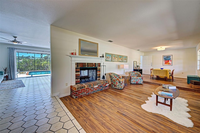 living room featuring a fireplace, a textured ceiling, ceiling fan, and wood-type flooring