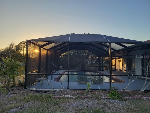 pool at dusk featuring glass enclosure and a patio area