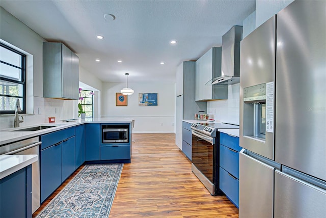 kitchen featuring light hardwood / wood-style flooring, blue cabinetry, decorative light fixtures, wall chimney range hood, and stainless steel appliances