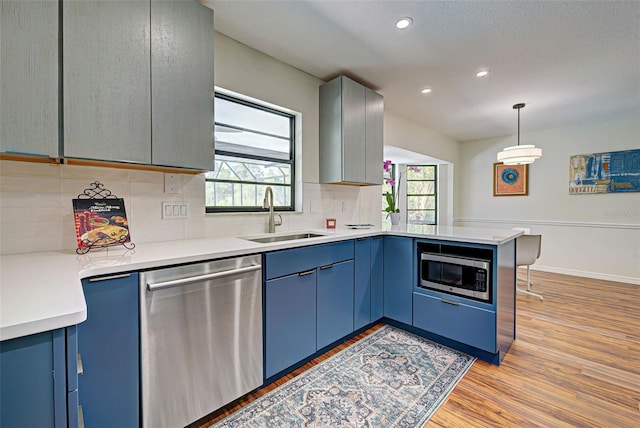 kitchen with appliances with stainless steel finishes, sink, light wood-type flooring, pendant lighting, and kitchen peninsula