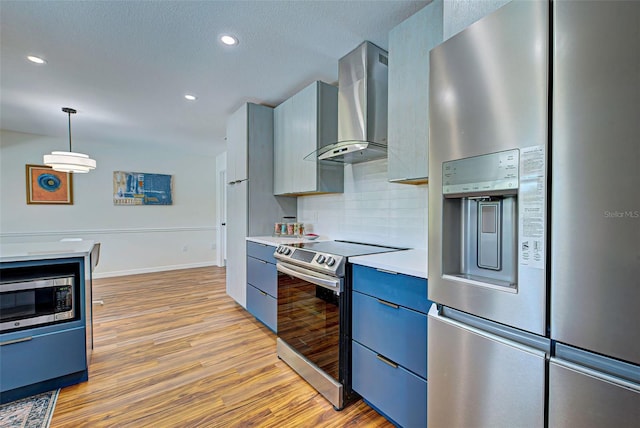 kitchen featuring hanging light fixtures, light hardwood / wood-style floors, backsplash, appliances with stainless steel finishes, and wall chimney range hood