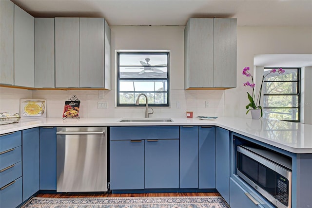 kitchen with appliances with stainless steel finishes, blue cabinets, backsplash, sink, and dark hardwood / wood-style floors