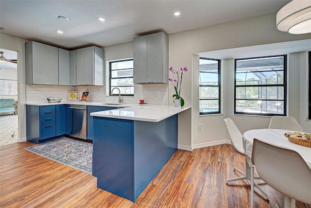 kitchen featuring sink, blue cabinetry, dishwasher, light hardwood / wood-style floors, and kitchen peninsula