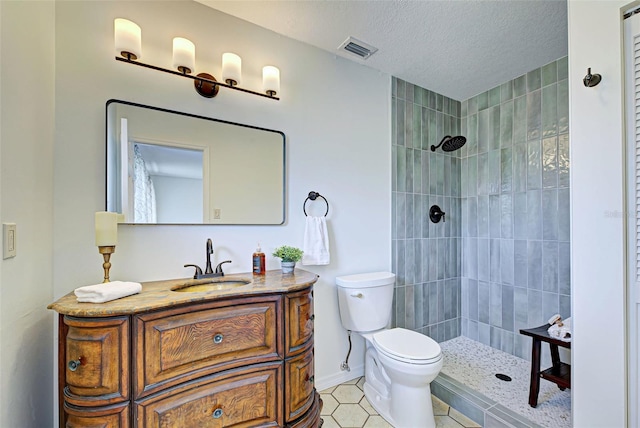 bathroom with a textured ceiling, toilet, vanity, and a tile shower