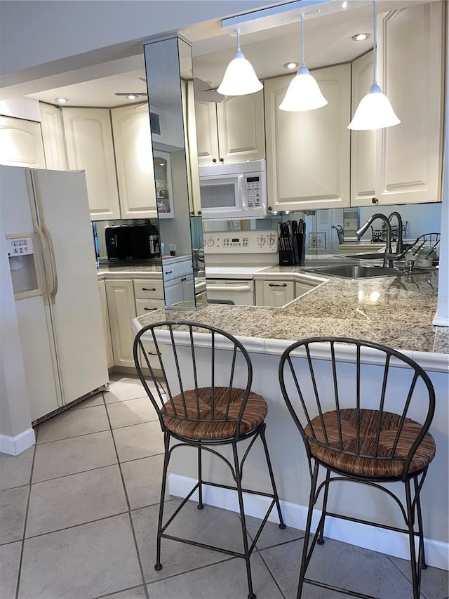 kitchen featuring a breakfast bar, white appliances, sink, light tile patterned floors, and kitchen peninsula