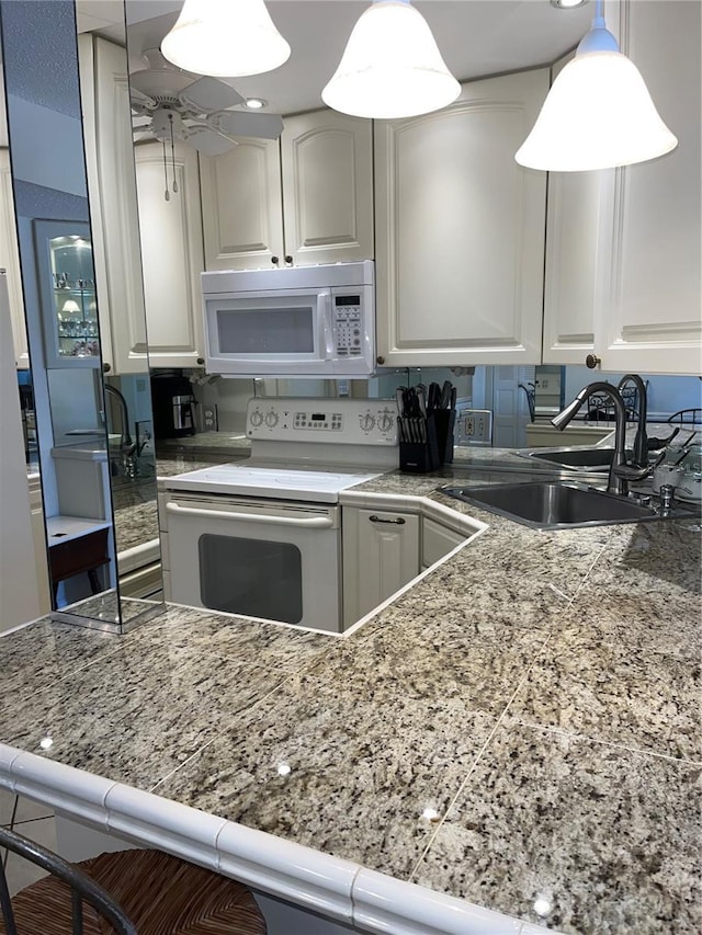 kitchen featuring white cabinetry, sink, hanging light fixtures, white appliances, and a breakfast bar