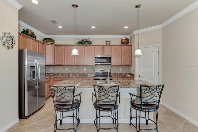 kitchen featuring hanging light fixtures, a center island with sink, stainless steel appliances, and light stone counters