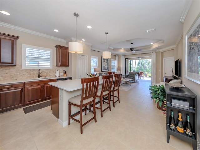 kitchen with a kitchen island, a breakfast bar, sink, a tray ceiling, and hanging light fixtures