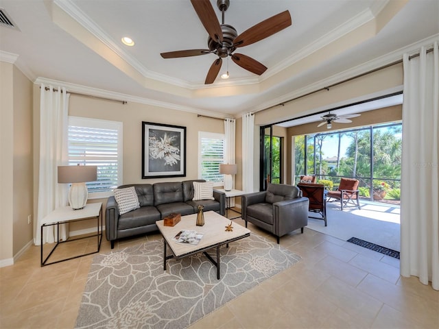 living room featuring ceiling fan, a tray ceiling, light tile floors, and ornamental molding