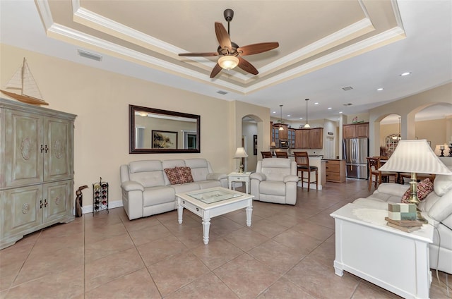 tiled living room with ornamental molding, ceiling fan, and a raised ceiling