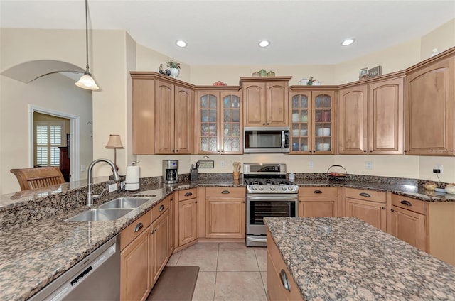 kitchen with decorative light fixtures, stainless steel appliances, sink, dark stone countertops, and light tile patterned floors