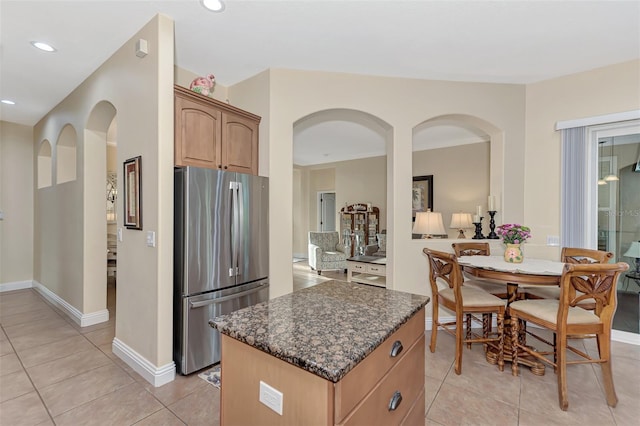 kitchen with a center island, dark stone countertops, stainless steel refrigerator, and light tile patterned floors