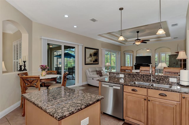 kitchen with a tray ceiling, sink, dark stone countertops, dishwasher, and a center island