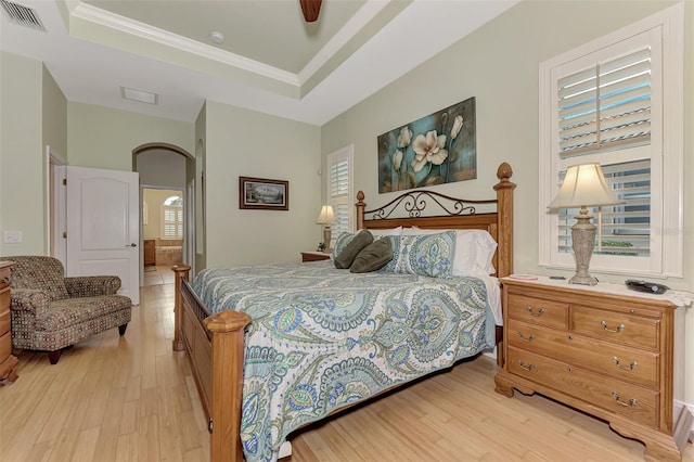 bedroom with light hardwood / wood-style floors, ceiling fan, and a raised ceiling